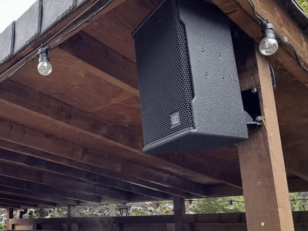 black wall mount pa sound system speaker on a wooden support for an outdoor bar at a wedding venue