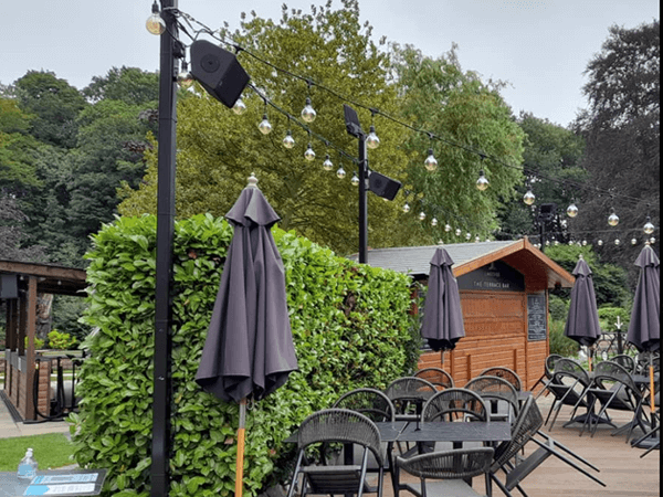 outdoor lighting and black speakers installed onto lighting poles around an outdoor seating area for a wedding restaurant venue